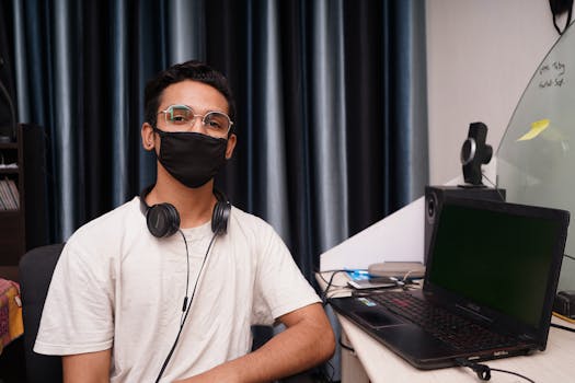 Man in White Crew Neck T-shirt Wearing Black Sunglasses Sitting Beside Table With Black Laptop